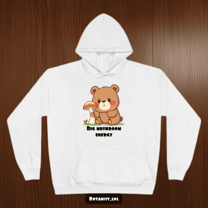 Funny hoodie showcasing a surprised bear with a curious gaze, captivated by the sight of a giant mushroom in the wilderness.