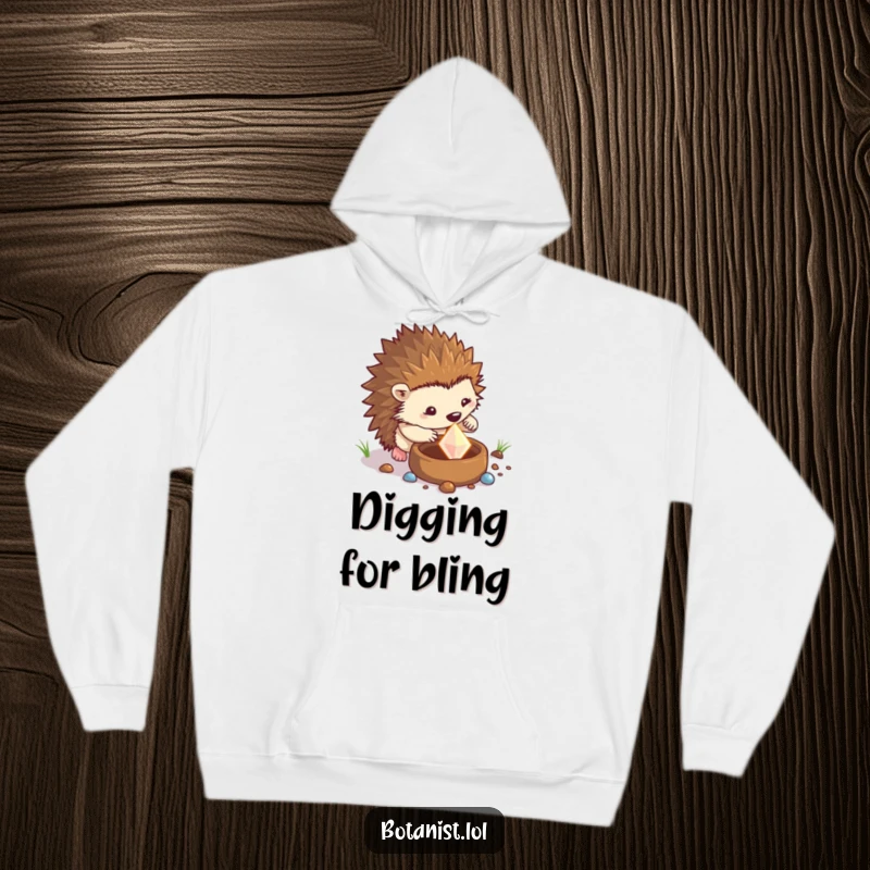 Funny hedgehog hoodie showing a determined hedgehog digging in a pot and finding a sparkling gem, perfect for cozying up after a big find.